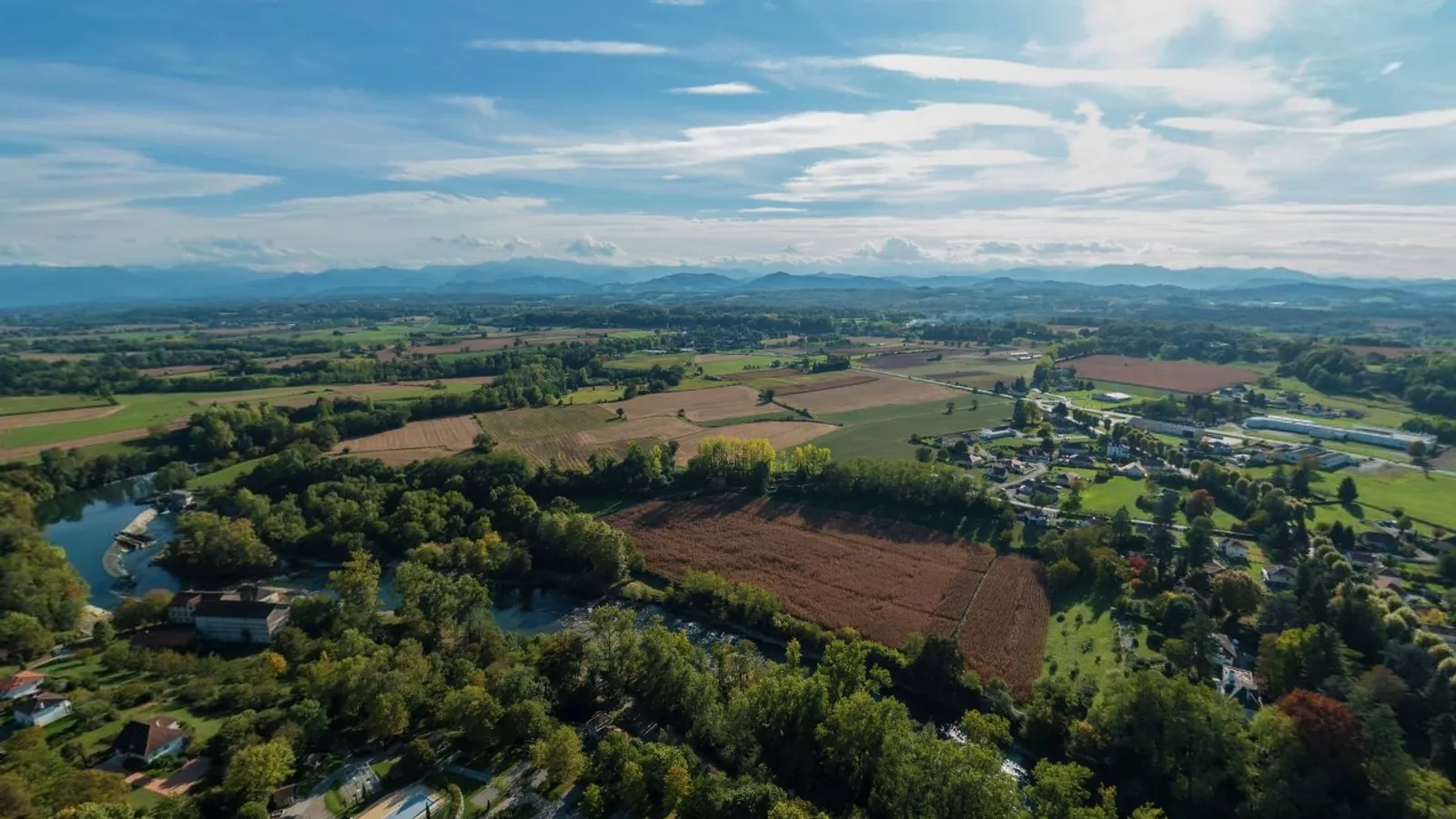 Vue du village de Sus dans la vallée du gave d’Oloron, coteaux boisés et Pyrénées en arrière-plan